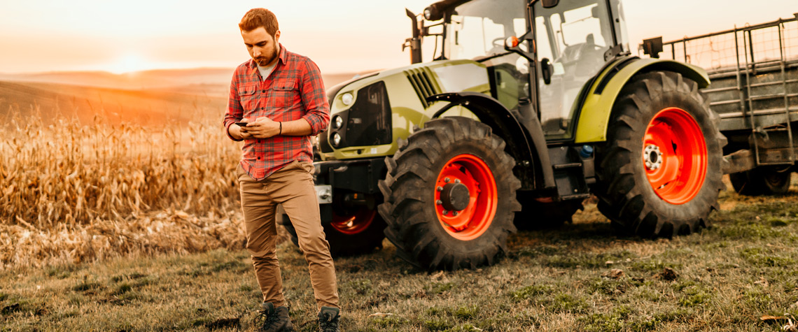 Farmer working on field using smartphone in modern agriculture - tractor background